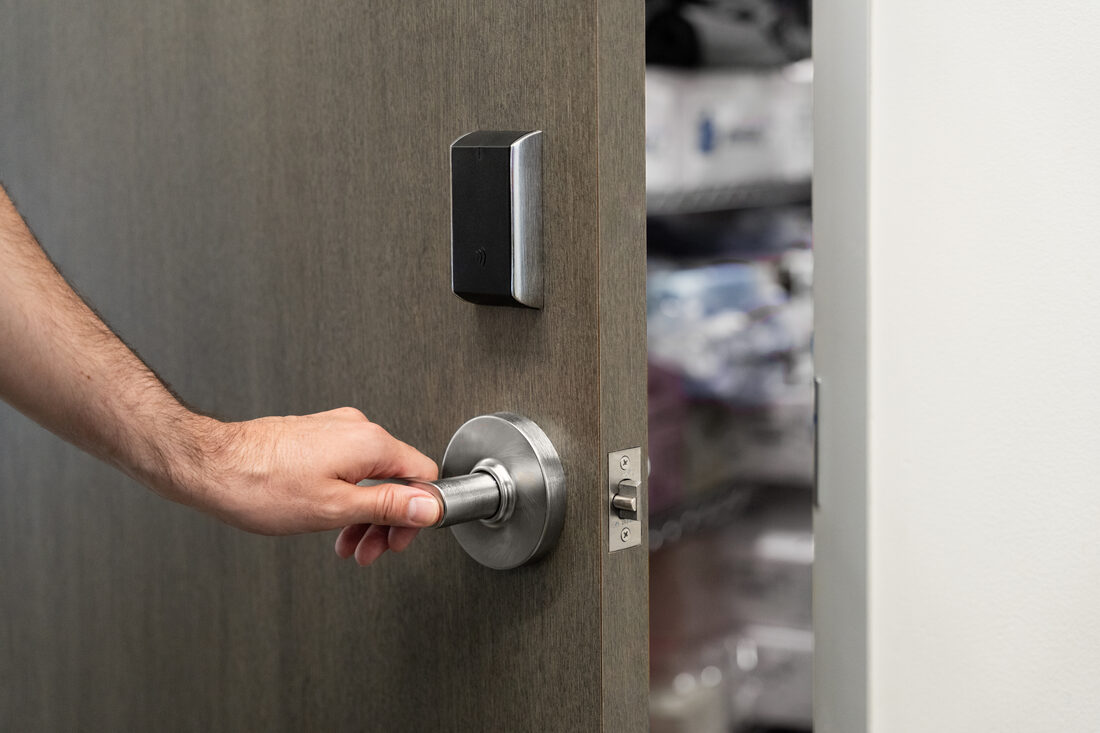 A hand on a door handle beside an access reader