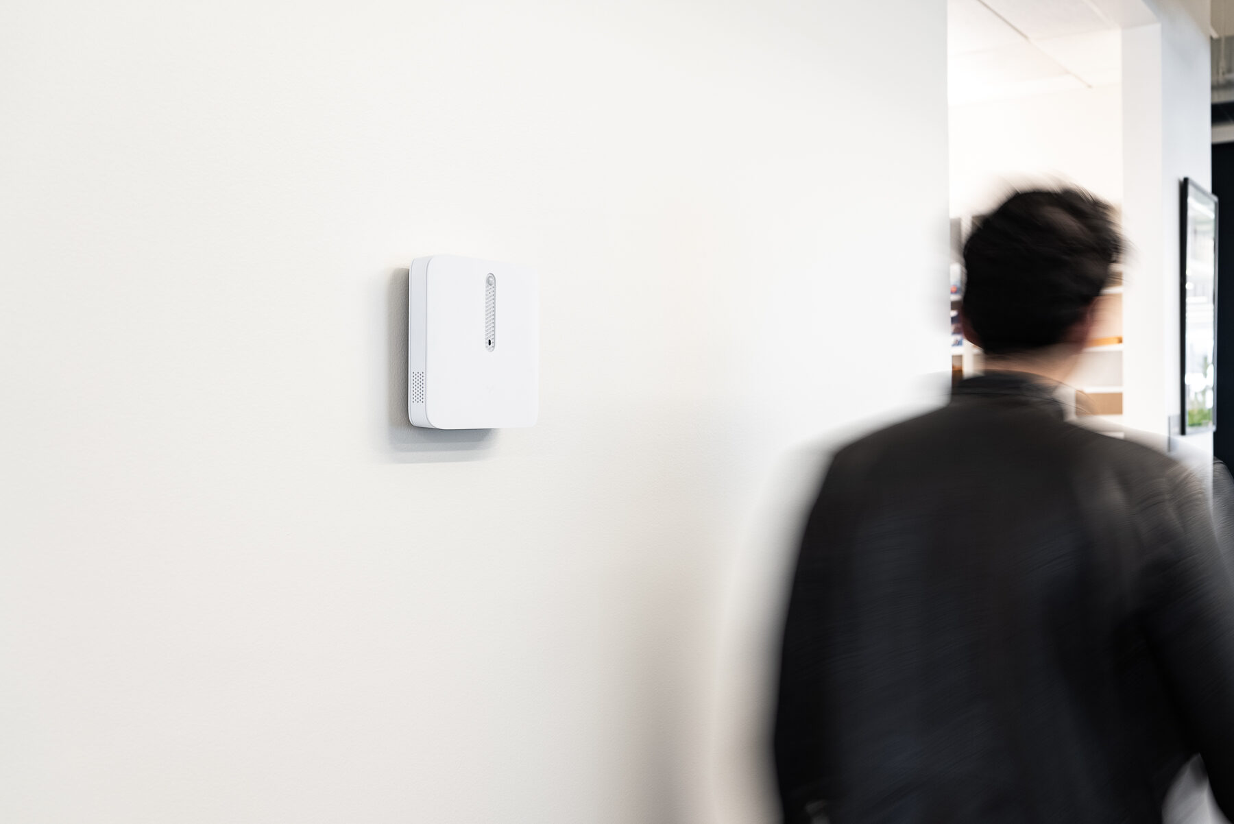 A person walking a corridor past a wall-mounted sensor