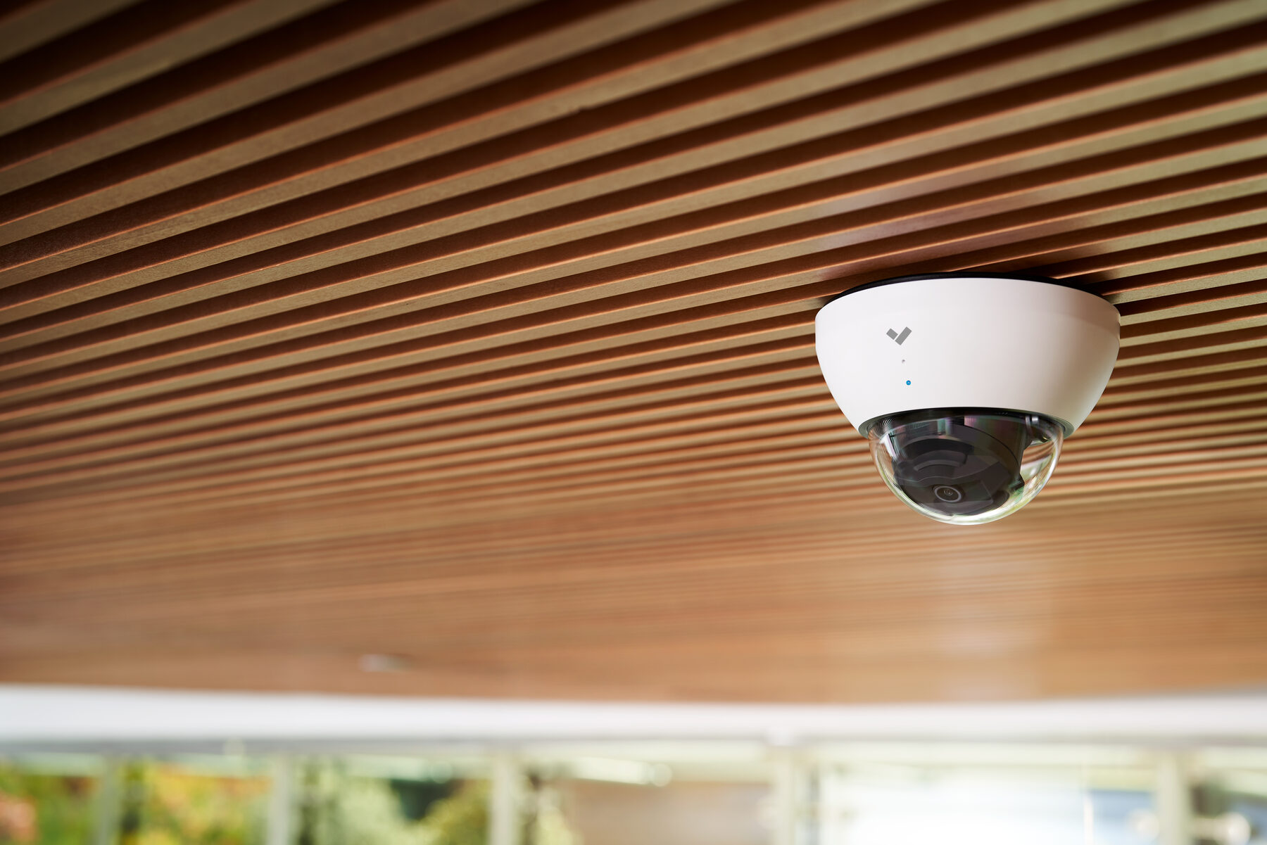 A discreet dome camera under a timber-slatted ceiling